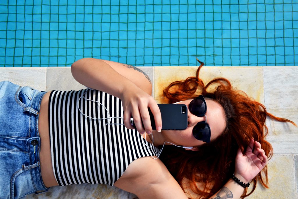 Jeune fille allongé au bord du piscine avec un téléphone à la main